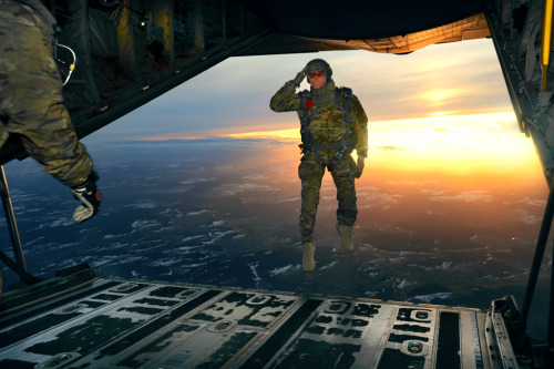A U.S. soldier salutes his fellow soldiers while jumping from a C-130 Hercules aircraft over a drop 