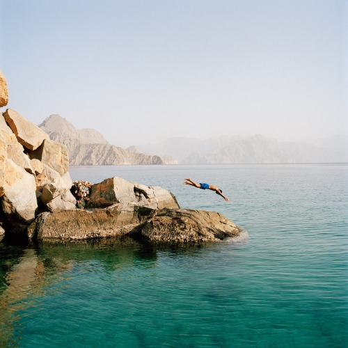 Young boy dives into the waters of the isolated northern Fjords near Khasab, Oman - photographed for