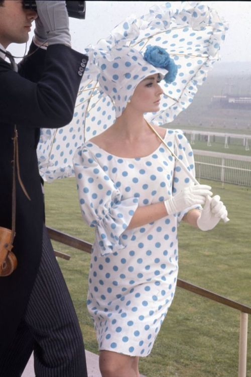 A woman poses with a polk-a-dot parasol and matching ascot dress while watching a race, 1965.