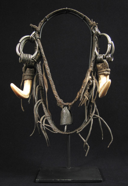 This is a leather headdress from Ethiopia with wart hog tusks at the side and an iron bell hanging a