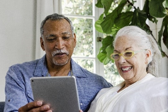 Older couple looking at tablet and smiling, caregivers, COVID-19