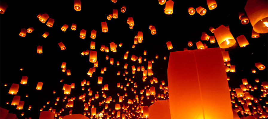 hundreds of floating lanterns being released, orange lights against a dark night sky