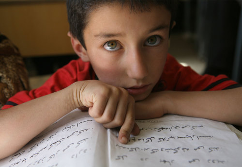 An Afghan Tajik boy reads a book in bomb-damaged Bazarak School, Afghanistan Source: Jean Chung