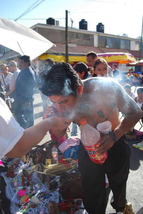 divinum-pacis: A man blowing smoke onto a miniature image of Santa Muerte.