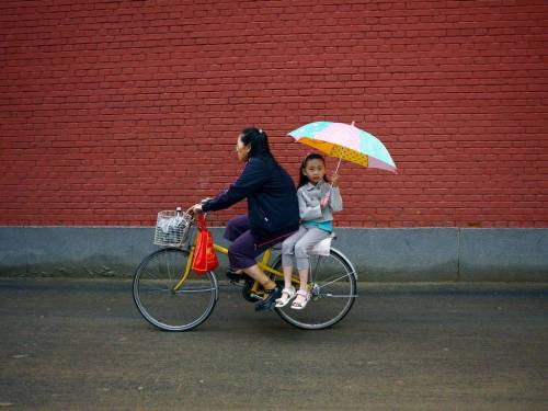 A girl holds an umbrella on the back of a bicycle along a road after school in Beijing on September 