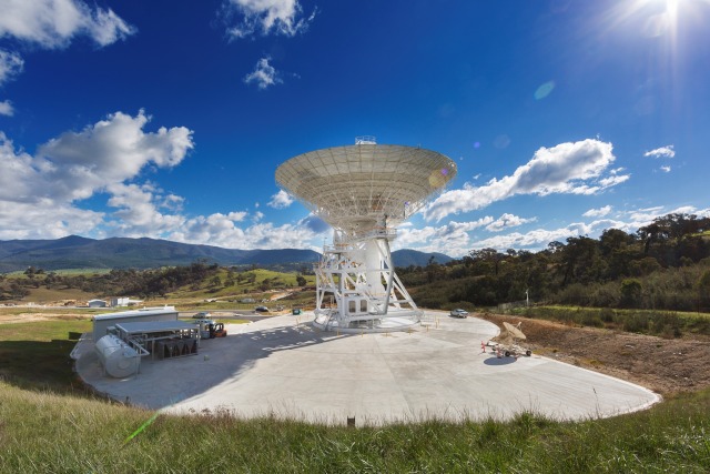 A giant 34-meter antenna, surrounded by rolling green hills, points towards a bright blue sky in Canberra, Australia. Credit: NASA