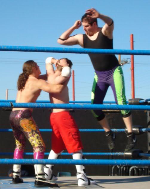 great picture! the two shirtless dudes go at it, back and forth, until the long haired dude takes control, maybe after a killer piledrive! he locks him in a fullnelson and motions for his partner to get on2 the top ropes. the bigger dude flys off...