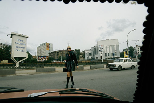 View on the New Russia: A car’s windshield, held in place by coins, frames a woman dressed to kill and a roadside sign reading, “the new generation chooses freedom.”Novosibirsk, Russia 