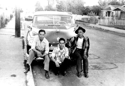 Silver Cariaso (left) and two other men lean on a car in a neighborhood in Watts, Los Angeles. 1959.