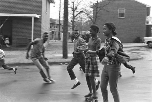 coolchicksfromhistory: Group of girls skating in the street in front of a public housing project on 