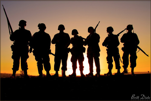 Reenactors from the WW2 82nd Airborne Living History Association stand with the setting sun behind t