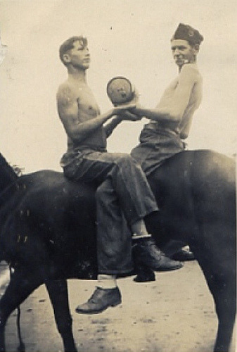 A vintage photograph of two men on horses, holding a large object.