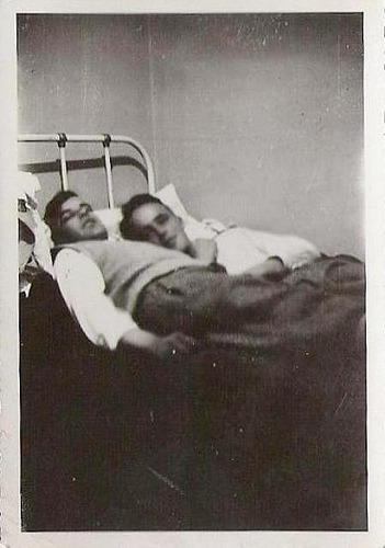 A vintage photograph of two men laying in bed together.
