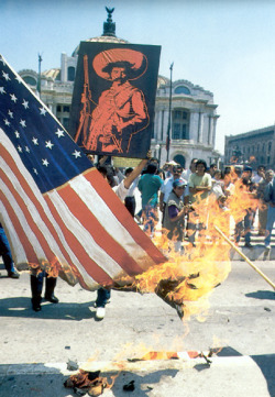 Zapatistas burn the American flag in protest because  American corporations are sucking dry third world countries of their natural resources.