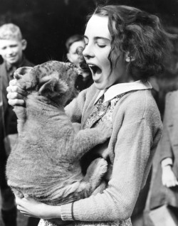   June Mottershead mimics her newly adopted lion cub at Chester Zoo in Cheshire. The lion has been adopted to save it from destruction because of lack of zoo funds, 30th September 1939. 