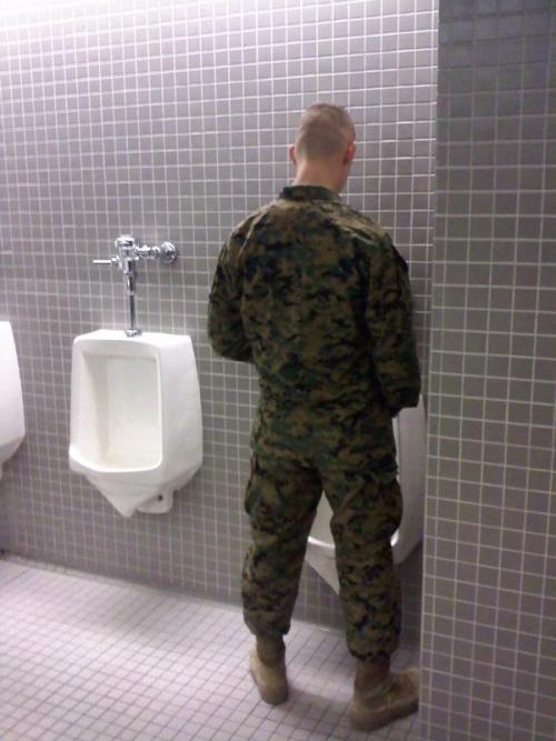 Military soldier taking a piss at a urinal, in a public bathroom.