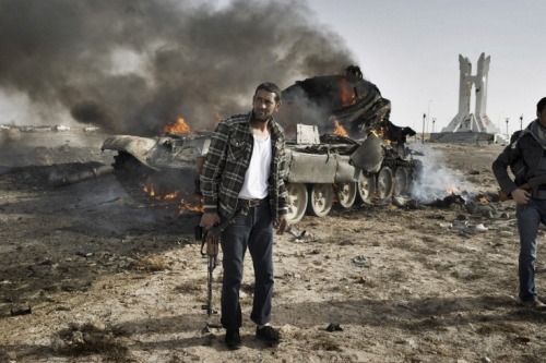 politics-war:Rebel fighters stand near a Gaddafi tank that was destroyed outside Ajdabiyah. 