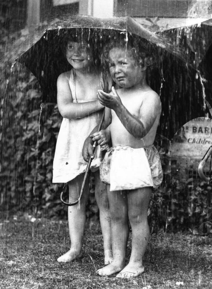 Two young children at Dr Barnardo’s sheltering under an umbrella from a garden shower.
Fox Photos/Getty Images, 21st June 1934