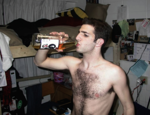 Hairy frat boy, drinking beer in his dorm room.