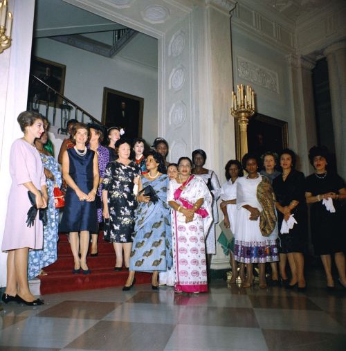 First Lady Jacqueline Kennedy hosts a tea party for wives of new ambassadors. The guests stand in front of the grand staircase in the Entrance Hall of the White House.
Guests include: Neila Zouiten Bourguiba (wife of Ambassador Habib Bourguiba, Jr....