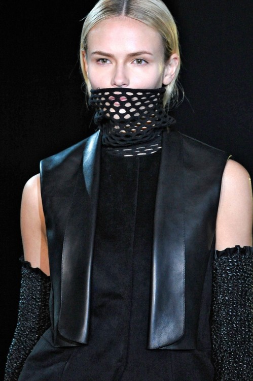 On the dark stage, models with their mouths covered by mesh turtlenecks marched in a square around b