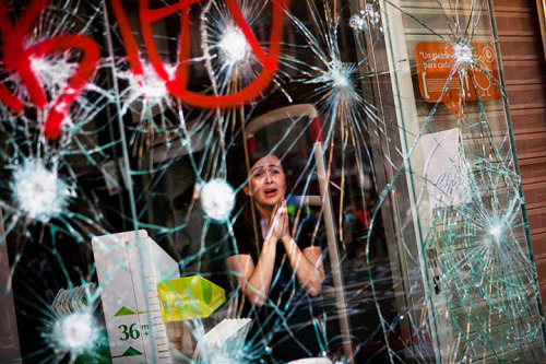 Mirian Burrueco stands behind the broken glass of her shop which was stormed by riots during the gen