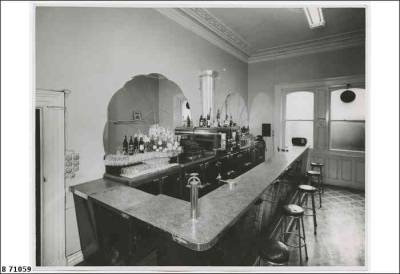 View of a bar in the Tavistock Hotel at 224 Rundle Street, Adelaide. It shows the bar with patrons’ stool, and glasses, flowers and cash register on the fridges behind the bar.
1952.