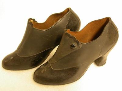 Pair of woman’s black rubber galoshes made by Dunlop Australia. Shiny rubber on vamp back and heel, scolloped edge on flat which is secured by single press stud with black jewel on top. Hand-writing on inside of sole.
The appearance of these shoes is...