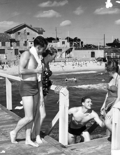 This photograph of Brighton Beath Baths shows John Marshall and Wendy Byrne standing on the boardwalk. Alan Trickey on the stairs and Kerry Lemon with one foot on stairs and one on boardwalk. John Marshall was a champion swimmer who later married...