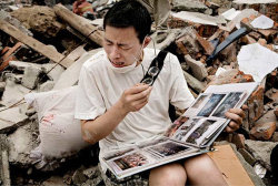 politics-war:  A man is crying while he flips through a family album he found in the rubbles of his old house. 