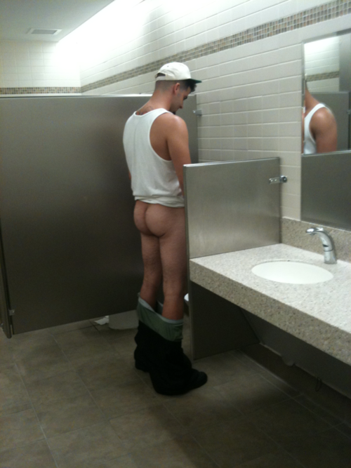 Frat bro pissing at a urinal, with his pants down at his ankles. 