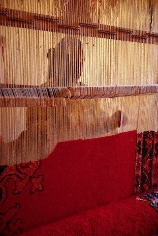 roxygen:Ouarzazate, Morocco — An Amazigh woman is silhouetted as she works at a loom with a pa