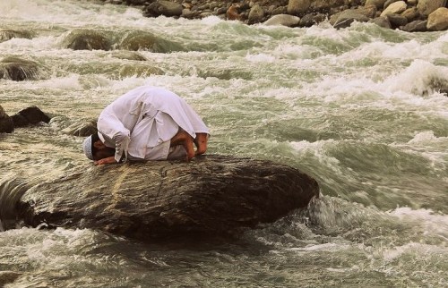 um-er: A man offers prayer on a stone in the fast flowing river Swat.