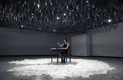  Beili Liu - The Mending Project (2011) “…Hundreds of Chinese scissors suspended from the ceiling in a shimmery cloud. The piece involved the artist sitting at a small black table, hand-mending patches of fabric together which visitors were encouraged