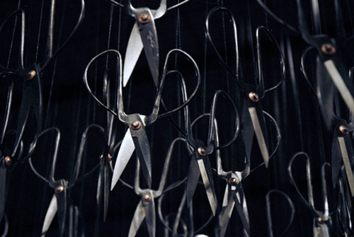  Beili Liu - The Mending Project (2011) “…Hundreds of Chinese scissors suspended from the ceiling in a shimmery cloud. The piece involved the artist sitting at a small black table, hand-mending patches of fabric together which visitors were encouraged