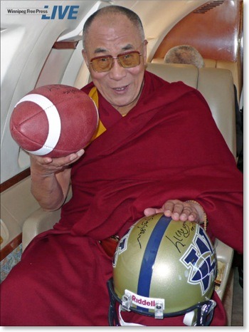 The Dalai Lama autographs a football and helmet for the Canadian Football Legue “Winnipeg Blue