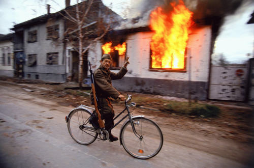 © Ron HavivA Serbian soldier cycles by a burning house on the destroyed streets of the Croatian city