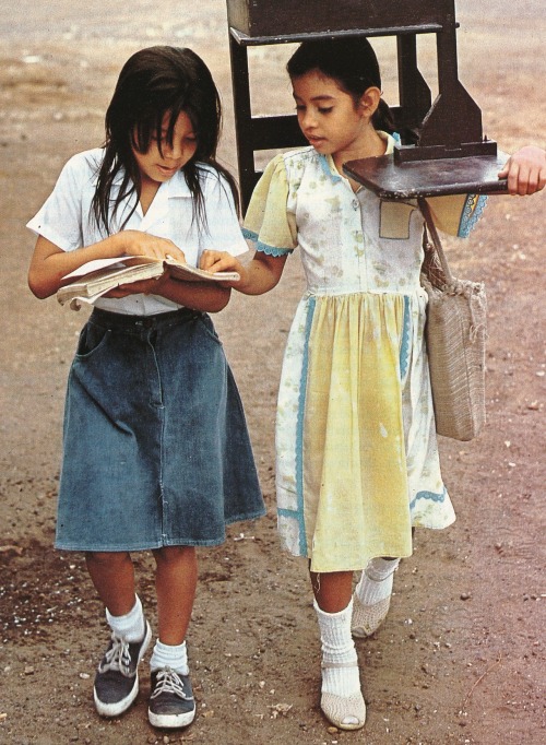 “With her school lacking desks, a student who has found one carries it home each day in a barr