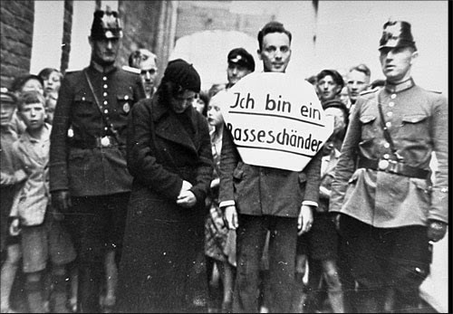 A German man caught having relations with a Jewish woman is publicly humiliated.  The sign reads &ld