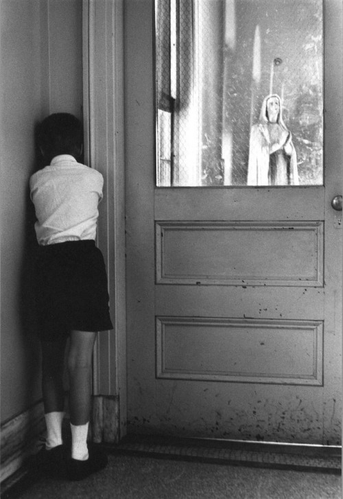 Student facing corner next to a door. Statue of Mary appears through window, St. Joseph’s School for the Deaf. Photographed by William Gedney, 1960.