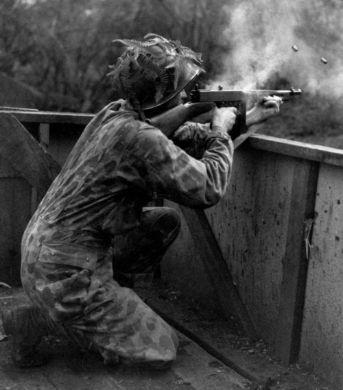 WWII USMC Frogskin Coveralls - A US Marine wearing his camouflage suit fires a Thompson sub-machine 