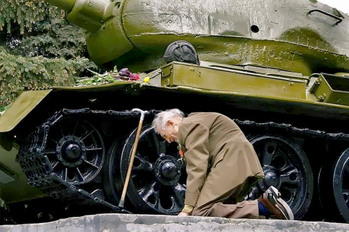A Russian war veteran kneels beside the tank he spent the war in, now a monument.