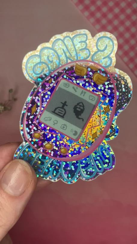 babbybratz:happy new year! huge thanks to everyone who interacted with my posts in 2022 🙏🏻 i recently reopened my etsy shop and have new sticker and print designs available, including this nostalgic sparkly tamagotchi design! my shop can be found